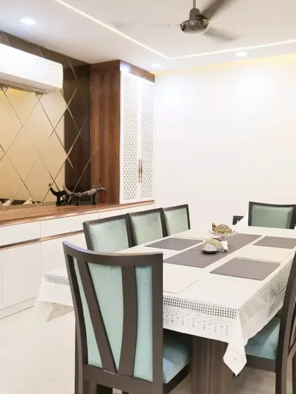 A dining area designed with a diamond-patterned mirror wall that visually expands the space and adds a touch of glamour, complemented by a sleek white and wood sideboard.