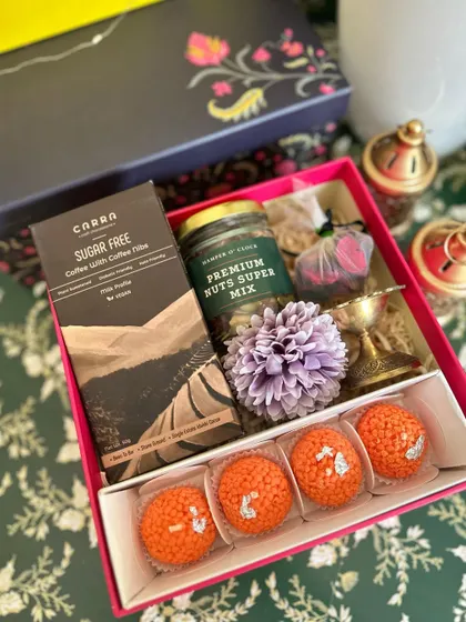 A close-up of the pink Diwali box, highlighting the premium nuts, brass diya, and other festive items.