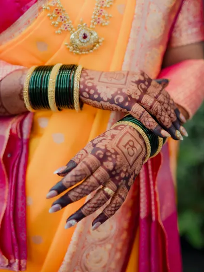The intricate details of a bride's attire are part of her story. This shot highlights the beautiful bridal mehndi design, featuring the couple's initials, and the traditional green glass bangles worn by Maharashtrian brides.