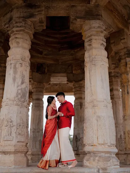 A couple stands between the ancient, carved pillars of a temple mandapam in Melukote, their connection as strong and timeless as the structure around them. A classic heritage pre-wedding photograph.