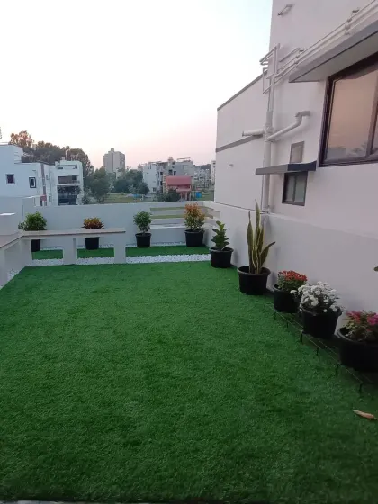 This view shows the other side of the rooftop garden, with potted plants lining the edge of the artificial lawn against the backdrop of the city.