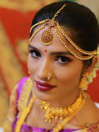 A striking portrait of a South Indian bride, looking directly at the camera, adorned in traditional gold jewelry.