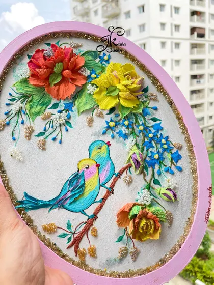 A lovely oval wall panel with two colorful birds on a branch, surrounded by red and yellow flowers and delicate blue blossoms.