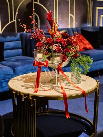 A close-up of a centerpiece for the European-themed night. A bouquet of red roses is accented with delicate red ribbons tied to the candle holders, a small detail that enhances the romantic theme.