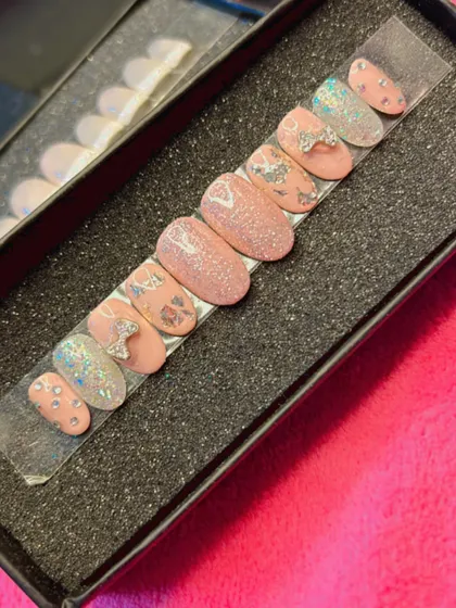 A playful and feminine press-on nail set in a rounded shape. It features a mix of glittery pink nails, nails with silver foil accents, and adorable 3D silver bows for a fun, textured look.