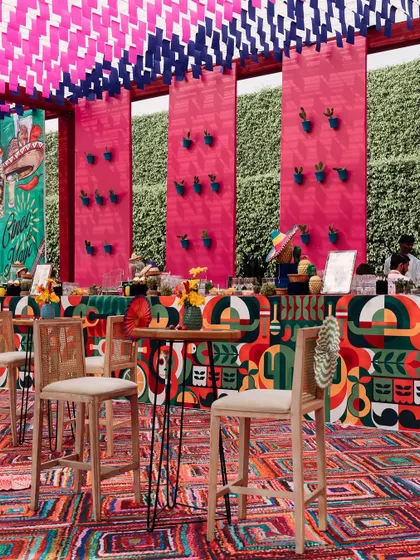 The bar area, with a custom-printed facade featuring bold, abstract patterns. The back wall is adorned with small potted cacti, and the high-top tables provide a casual spot for guests to mingle.