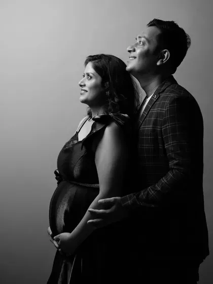 A hopeful black and white portrait of an expecting couple looking up and away. The dramatic studio lighting creates a sense of looking towards the future together.