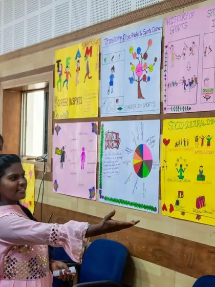 A graduate proudly explains her group's project work to an attendee. This moment highlights the practical application of their learning, as they articulate complex ideas about sustainable development and social impact through sports.