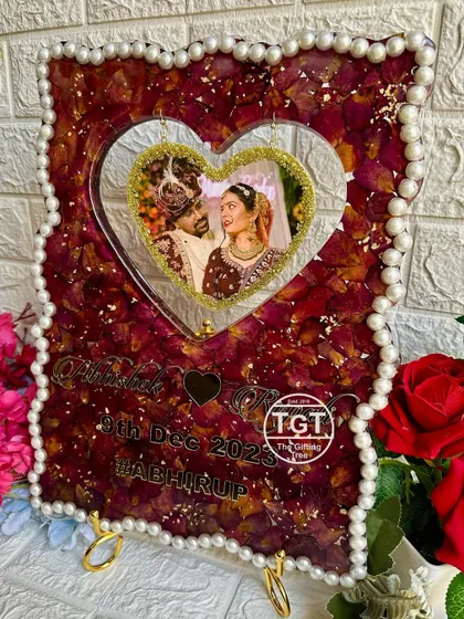 This 12x16 inch frame features a hanging heart for the couple's photo, surrounded by preserved red rose petals and gold flakes for a luxurious feel.