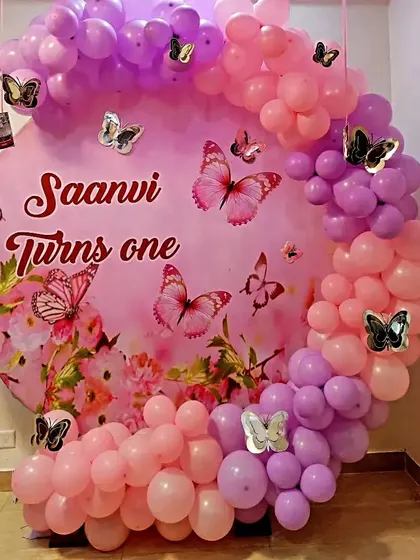 A pretty butterfly theme for a first birthday, featuring a personalized pink backdrop and a pink and purple balloon arch.
