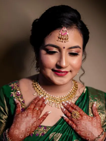 A quiet moment of reflection for this beautiful bride before her engagement. The makeup features soft, rosy tones on the eyes and lips, which perfectly complements her emerald green and gold silk saree.