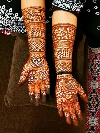 A beautiful party henna design with circular mandala-like patterns on the palm and geometric bands on the arms.