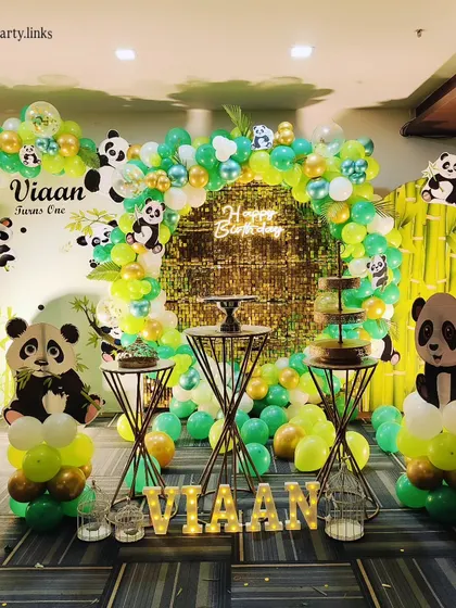 For this adorable Panda-themed first birthday, I used a green and gold color scheme. The setup features a gold shimmer wall, bamboo-like backdrops, cute panda cutouts, and light-up letters for the name.