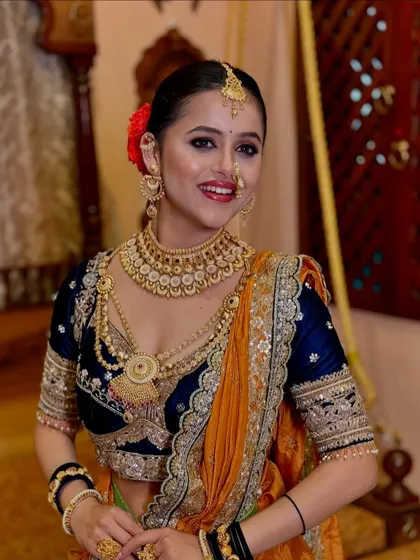 A stunning Maharashtrian bridal look featuring a navy blue and orange Nauvari. The drape is designed to highlight the rich colors and intricate gold work.