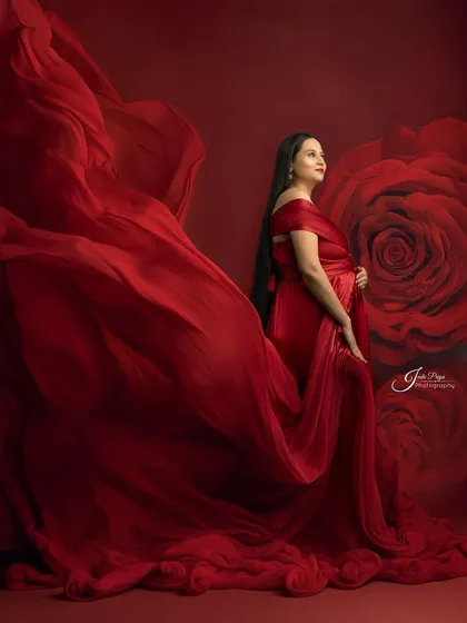 A variation of the fabric-tossing technique, this time against a rich red background with a subtle rose pattern. The mom-to-be looks up, creating a hopeful and elegant pose.