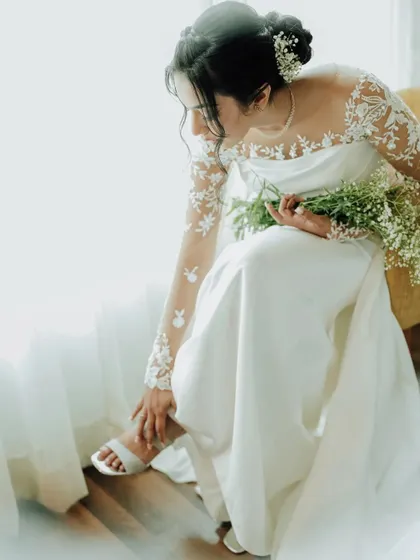 A beautiful, artistic shot of the bride getting ready. The focus on her adjusting her shoe, with the delicate details of her dress, creates an elegant and intimate portrait.