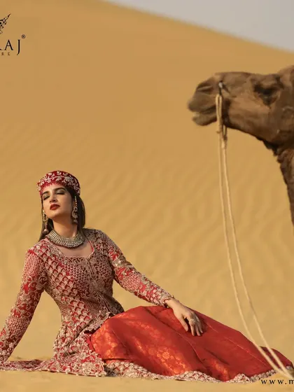 An artistic shot of the rose-gold Indo-Western outfit, featuring a long tail and a traditional cap, set against a dramatic desert backdrop.
