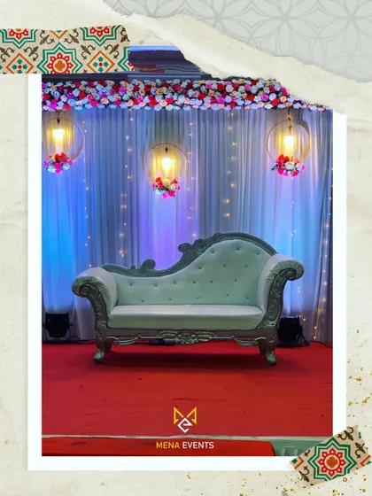 A simple yet elegant stage setup for a reception or engagement. The soft drapes, hanging floral lights, and classic lounge sofa are illuminated with gentle uplighting to create a warm and inviting focal point.