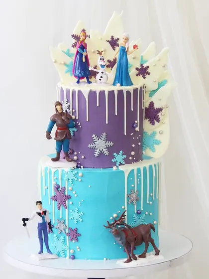 A grand "Frozen" castle cake for a true fan. This multi-tiered creation features all the main characters, including Elsa, Anna, Kristoff, Sven, and Olaf, set against a wintery drip cake with edible snowflakes.