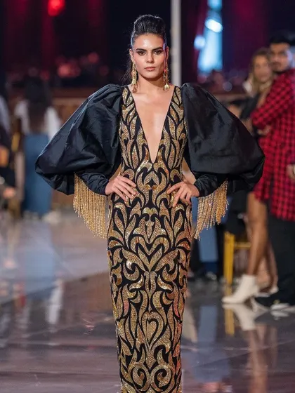A full-length shot of a model on the runway for the Abu Jani Sandeep Khosla show. The makeup features a strong, defined eye and contoured cheekbones to match the dramatic gown.