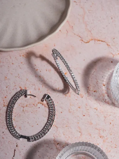 Minimal and aesthetic on point. These sparkling diamond hoops are styled on a textured marble surface with glass elements to create a clean, modern, and luxurious feel.