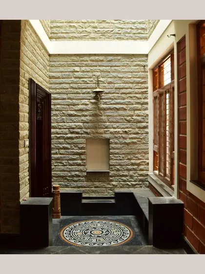 A quiet indoor nook with rough stone walls and a beautiful floor mandala, illuminated by a skylight, creating a perfect spot for contemplation.