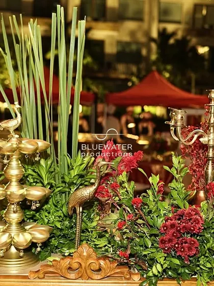 A traditional brass 'diya' stand is incorporated into a floral arrangement, blending sacred elements with beautiful decor.