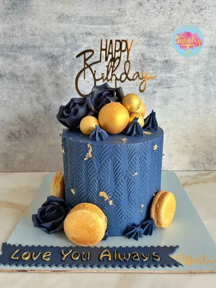 A stunning navy blue cake with a modern texture, adorned with golden macarons, spheres, and navy roses.