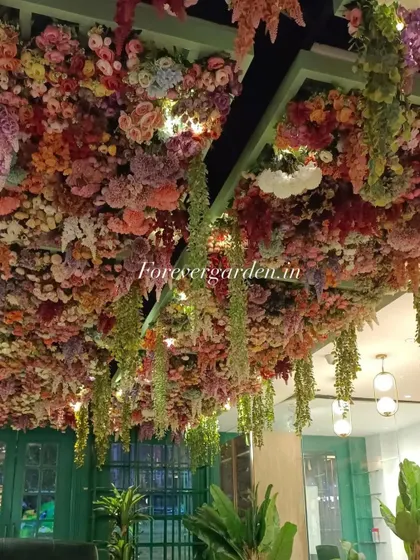 An incredibly dense and colorful floral ceiling, packed with a variety of artificial flowers and hanging greenery, creating a fantasy garden feel for this venue.
