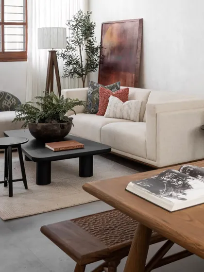 A closer view of the living area, focusing on the matte-black coffee table, the tripod floor lamp, and the mix of ikat, boucle, and handloom striped cushions on the sofa.