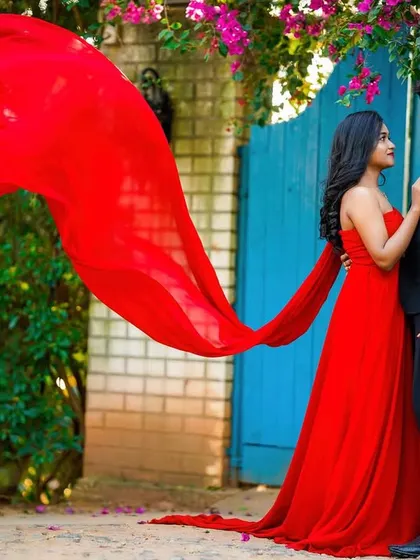 A vibrant pre-wedding shot with the bride's flowing red dress creating a stunning visual against a blue gate.