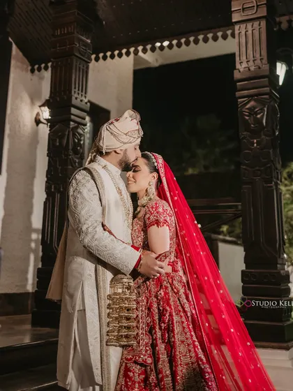 A romantic portrait of the couple, with the groom kissing the bride's forehead, her red veil adding to the classic look.