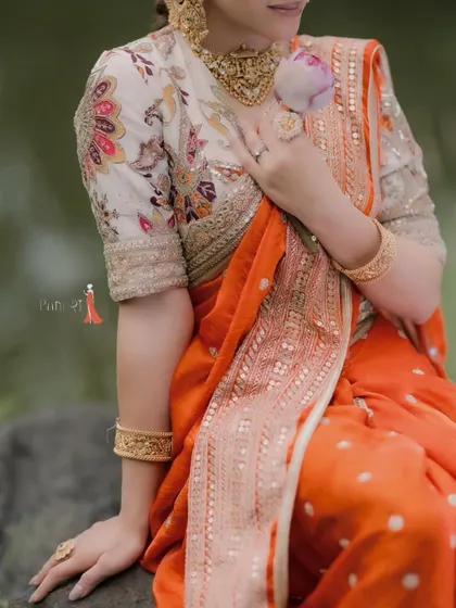 A close-up of a vibrant orange saree paired with a floral print blouse. The detailed border work on the saree and the intricate embroidery on the blouse showcase the level of craftsmanship in each piece.