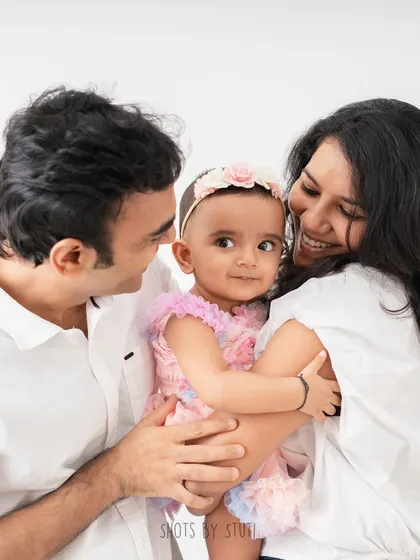 A beautiful family portrait, with the parents looking lovingly at their daughter. The soft expressions and gentle hold create a feeling of warmth and intimacy.