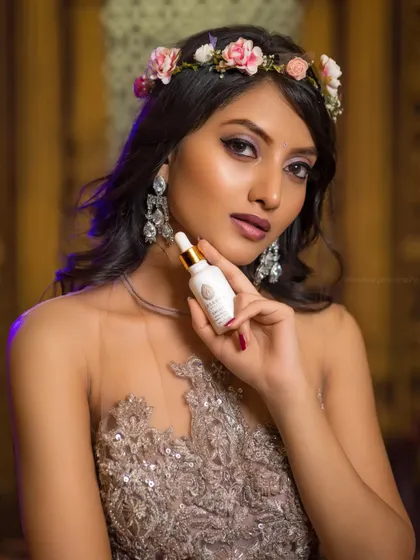 A commercial beauty shoot for Apsaras Beauty, where the model holds the product prominently. The floral crown and elegant setting create a narrative of natural beauty.