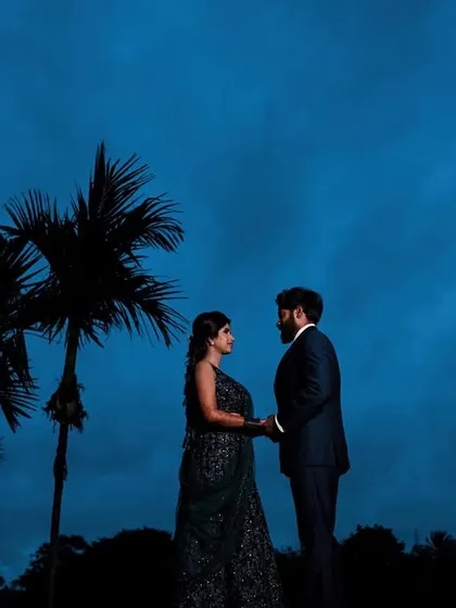 A dramatic silhouette of a couple against a deep blue twilight sky, framed by palm trees.