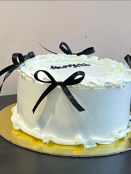 Embracing the trendy "coquette" aesthetic, this elegant white cake is adorned with delicate piping and simple black bows for a chic and fashionable look.
