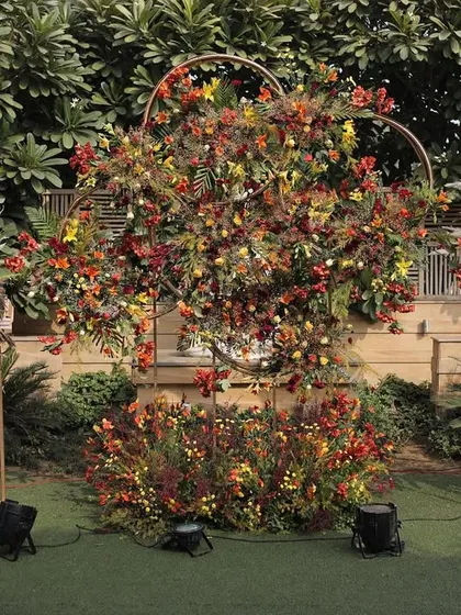 A photo backdrop inspired by the colors of autumn, featuring a heart-shaped frame filled with rustic, warm-toned florals and pampas grass.