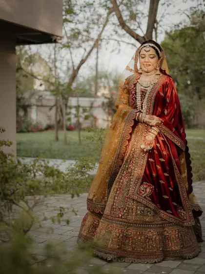A full-length portrait capturing the grandeur of the bride's velvet lehenga and the elegance of her pose in a garden pathway.