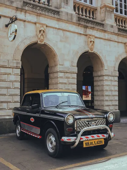 A frontal shot of a Premier Padmini taxi, highlighting its unique grille and the textures of the heritage building behind it.