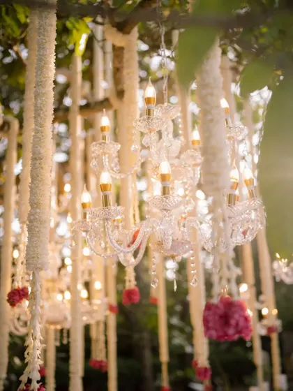 Crystal chandeliers hanging from a tree amidst jasmine garlands, creating a magical, open-air ballroom effect for an evening wedding.