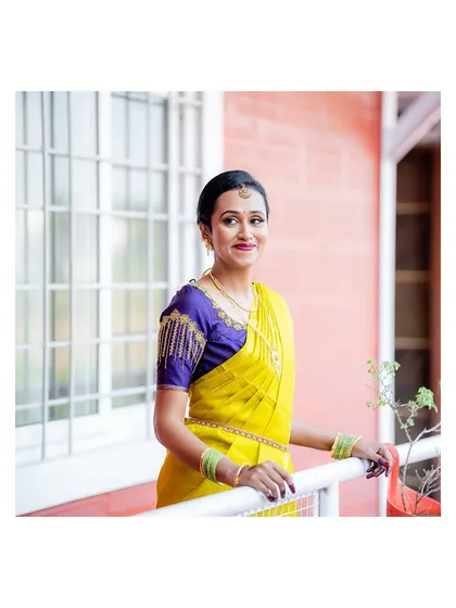 A beautiful portrait of the bride in a vibrant yellow Kanjeevaram saree, smiling on a balcony.