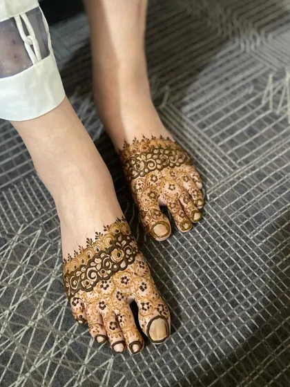 A delicate and simple henna design for feet, featuring a floral band across the top of the foot and detailed toe work.
