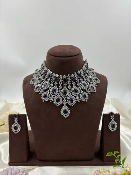 A heavy, silver-plated AD necklace set with a peacock-inspired feather design. This statement piece is available in blue, green, pink, and all-white.