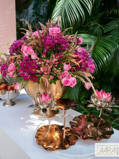 A close-up of the decor details from our 'Pomegranate Spring' theme. A brass urn filled with wild pink flowers sits beside ornate silver lotus candle holders, blending rustic charm with elegant details.