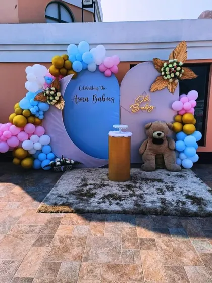 A modern and stylish baby shower backdrop on a patio, using geometric shapes, a custom sign, and a large teddy bear.