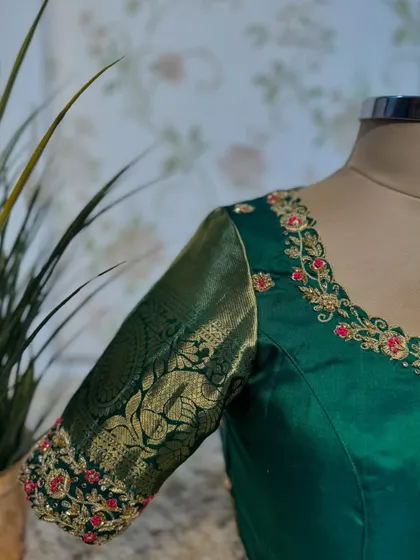 A close-up of the sleeve of the green blouse, showing the delicate red and gold floral embroidery.