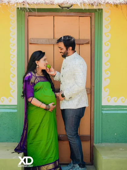 A playful and sweet moment during a traditional themed shoot, where the partner offers a raw mango to the mother-to-be.
