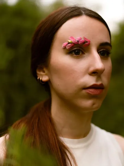 A close-up from a conceptual portrait session in a natural setting. The addition of flower petals on the eyebrow adds a touch of surreal beauty to the shot.