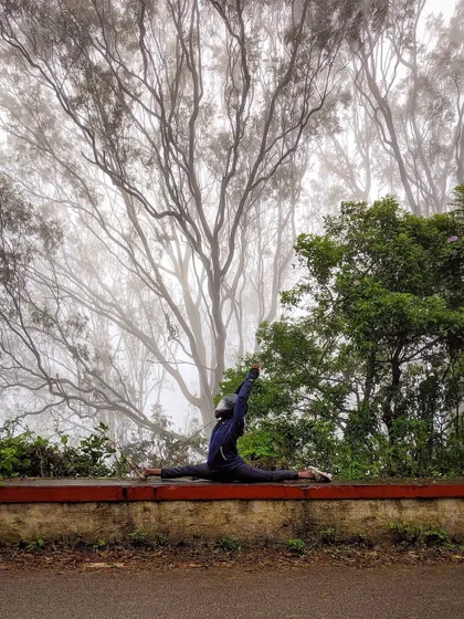 A moment of liberation in Hanumanasana, framed by the misty, skeletal trees of Nandi Hills. The atmosphere adds a layer of magic to the physical posture.